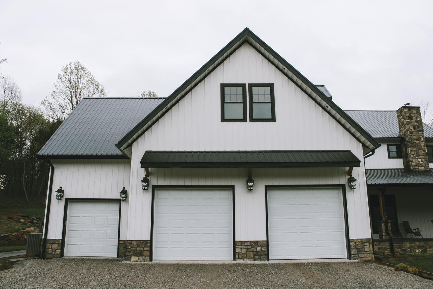 Large three-car garage with white board and batten metal siding, black roof, and modern exterior finishes
