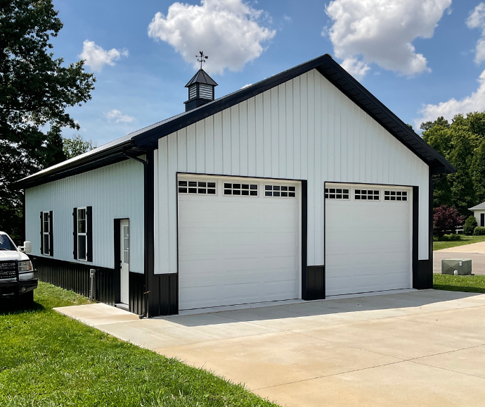 Large two-door garage with black roof, white siding, and a black-and-white cupola for decorative ventilation