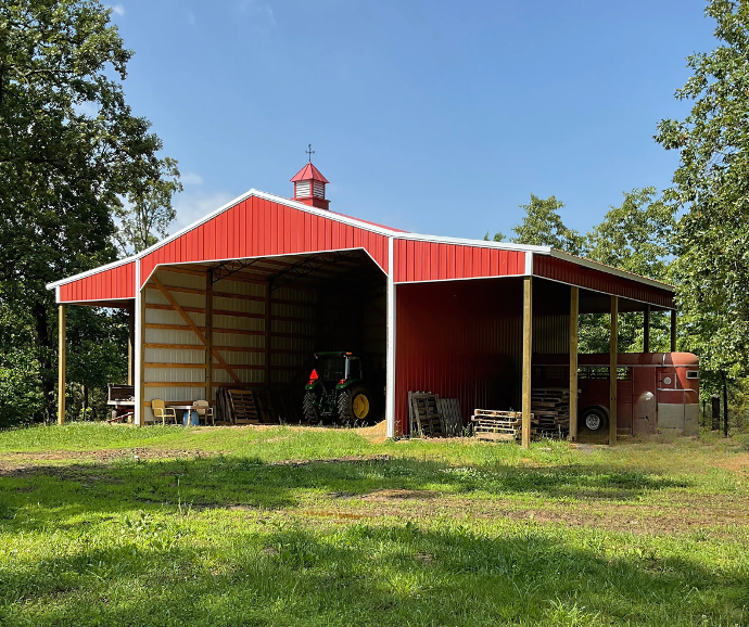 Open-sided red hay barn with white trim and a red-and-white rooftop cupola for classic barn style