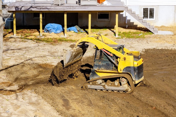 Large construction vehicle grading site by leveling and preparing dirt for building foundation