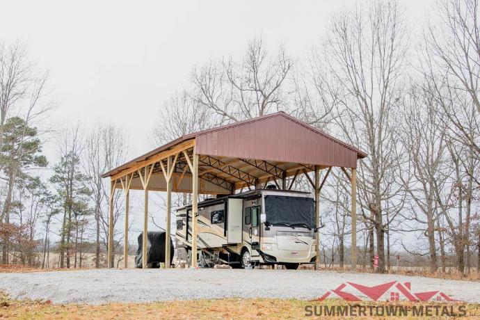 Hay barn with red siding on top and an RV parked underneath