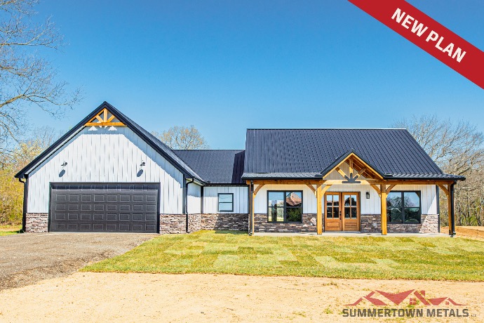 White-sided Mini Pettus barndominium with dark roof, large black double garage doors, wood and stone exterior accents